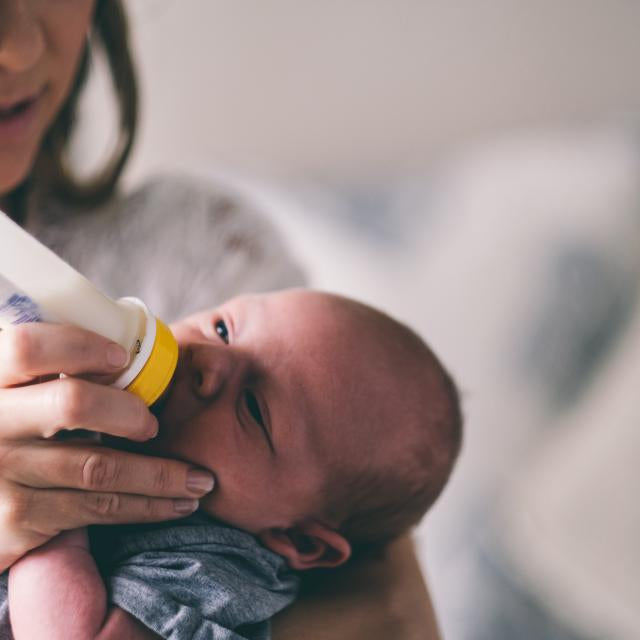 Mamma som matar bebis med nappflaska