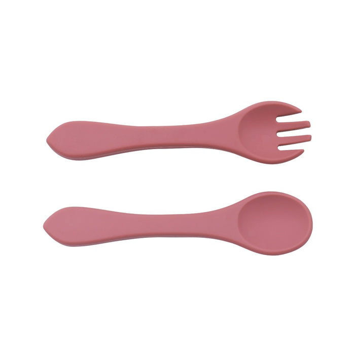 Två rosa Barnbestick Silikon redskap, märkta av Toddlers Of Sweden, vilande på en vit bakgrund. Det ena redskapet är en spork med tre pinnar, medan det andra är en standardsked. Båda BPA-fria redskapen har lätt böjda handtag för enkelt grepp.