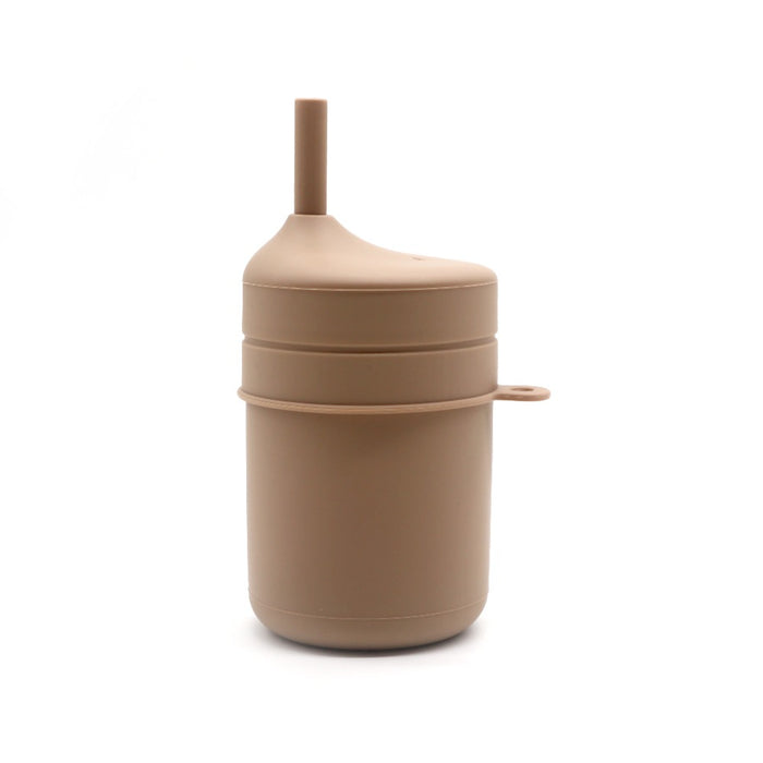 TOS Silikon Pipmugg Sugrör av Toddlers Of Sweden är avbildad mot en vit bakgrund. Denna beige, cylindriska sippy-kopp kommer med lock och inbyggt sugrör, med en enkel och värmetålig design. Den har ett litet handtag på sidan och har en slät finish.